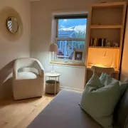 Small Bedroom Gemütlich eingerichtetes kleines Zimmer mit hellem Sessel, Schreibtisch und Fenster mit Blick nach draußen.
