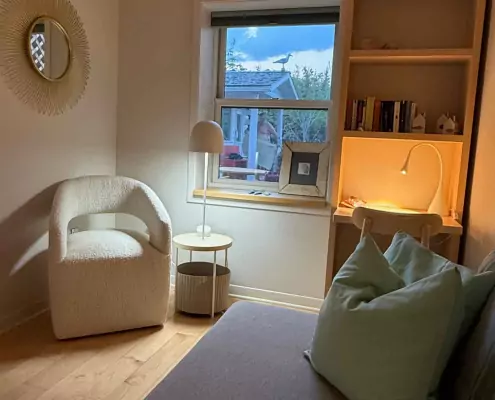 Small Bedroom Gemütlich eingerichtetes kleines Zimmer mit hellem Sessel, Schreibtisch und Fenster mit Blick nach draußen.