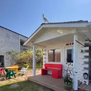 Finnische Sauna Weiße Holzhütte im Garten mit roter Bank und bunten Gartenmöbeln – eine finnisch inspirierte Sauna oder Gästehaus-Atmosphäre.