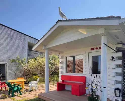 Finnische Sauna Weiße Holzhütte im Garten mit roter Bank und bunten Gartenmöbeln – eine finnisch inspirierte Sauna oder Gästehaus-Atmosphäre.