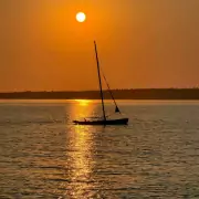 Sonnenaufgang über Port Mouton Island Ein Segelboot gleitet bei Sonnenuntergang über das ruhige Wasser, die Sonne spiegelt sich im Meer.
