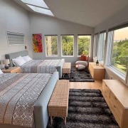 Master Bedroom Großzügiges Schlafzimmer mit zwei Doppelbetten, großen Fenstern und Blick ins Grüne bei Sonnenuntergang.