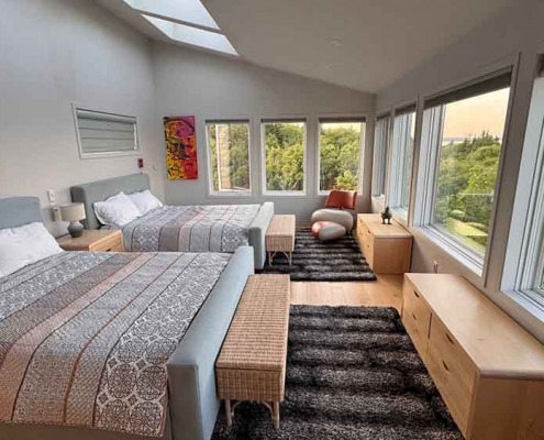 Master Bedroom Großzügiges Schlafzimmer mit zwei Doppelbetten, großen Fenstern und Blick ins Grüne bei Sonnenuntergang.