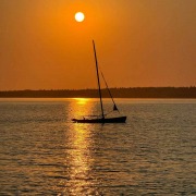 Morning has broken A sailboat glides across calm water, the sun reflecting on the sea.