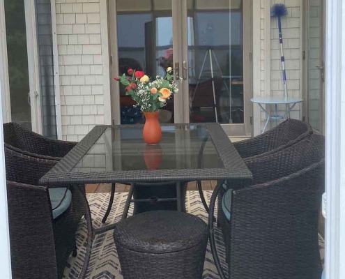 Pièce vitrée avec vue sur la mer, table dressée avec mobilier en rotin et bouquet de fleurs fraîches.