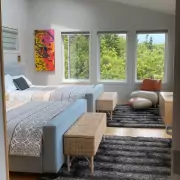 Modernes Schlafzimmer mit zwei Doppelbetten Modernes Schlafzimmer mit zwei Doppelbetten, großflächigen Fenstern und weitem Blick ins Grüne bis zum Meer, dekoriert mit einem farbenfrohen Kunstwerk.