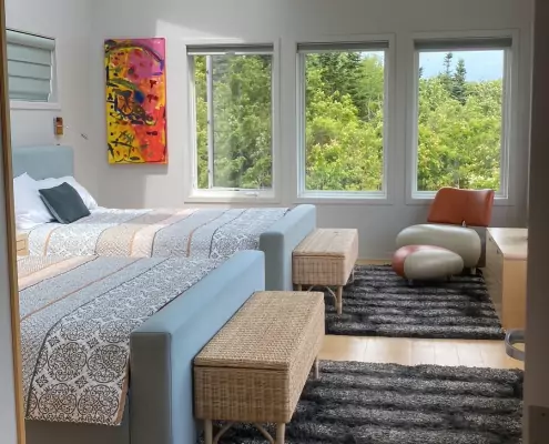 Modernes Schlafzimmer mit zwei Doppelbetten Modernes Schlafzimmer mit zwei Doppelbetten, großflächigen Fenstern und weitem Blick ins Grüne bis zum Meer, dekoriert mit einem farbenfrohen Kunstwerk.