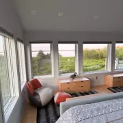 Schlafzimmer mit Panoramafenstern Schlafzimmer mit Panoramafenstern und Blick auf grüne Natur und Wasser, gemütlicher Sessel mit Hocker am Fenster, moderne Einrichtung.