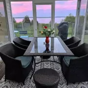 Abendstimmung auf der Terrasse Überdachte Terrasse mit Glastisch und Korbstühlen, Blick auf das Meer und rosa Abendhimmel.