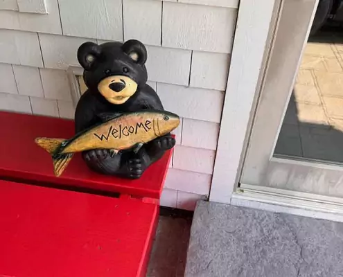 Herzlich Willkommen Deko-Bär mit Fisch in den Pfoten und dem Schriftzug „Welcome“ – herzlicher Willkommensgruß vor dem Eingang.