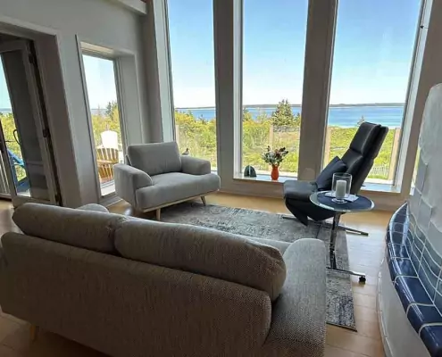 Gemütliches Wohnzimmer Gemütliches Wohnzimmer mit weitem Blick auf die Küste, stilvolle Einrichtung mit grauen Sesseln und einem schwarzen Relaxsessel vor einer großen Fensterfront.
