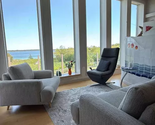 Heller Wohnbereich mit Blick aufs Meer Heller Wohnbereich mit bodentiefen Fenstern und Meerblick, ausgestattet mit modernen Sesseln und einem hellen Holzboden.